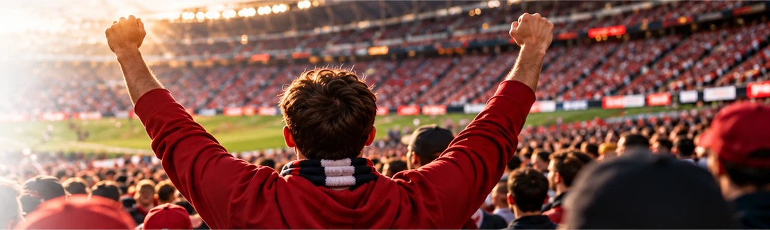 A fan in a red hoodie raises both fists in a packed stadium